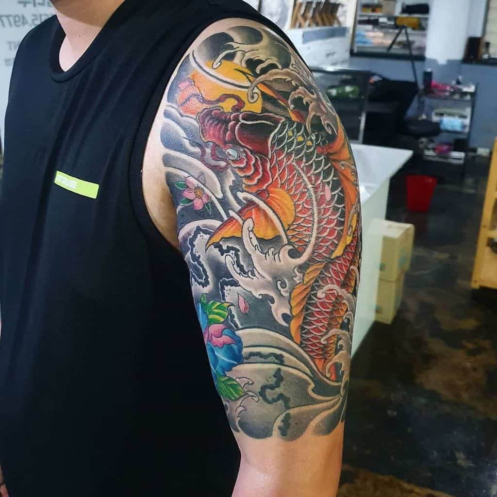Arm tattoo featuring a colorful koi fish with waves and flowers on an upper arm