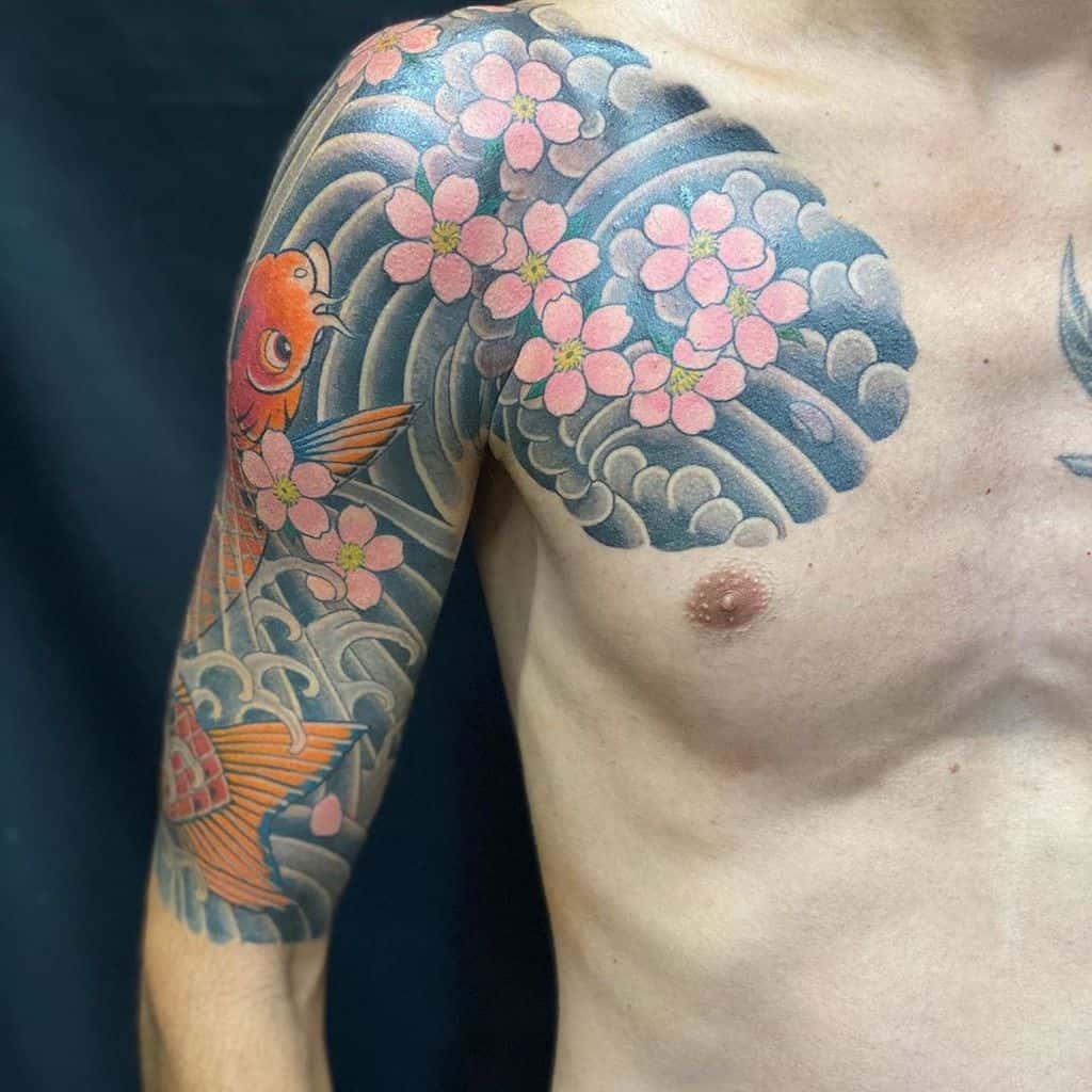 Tattooed shoulder and arm with koi fish, cherry blossoms, and water waves