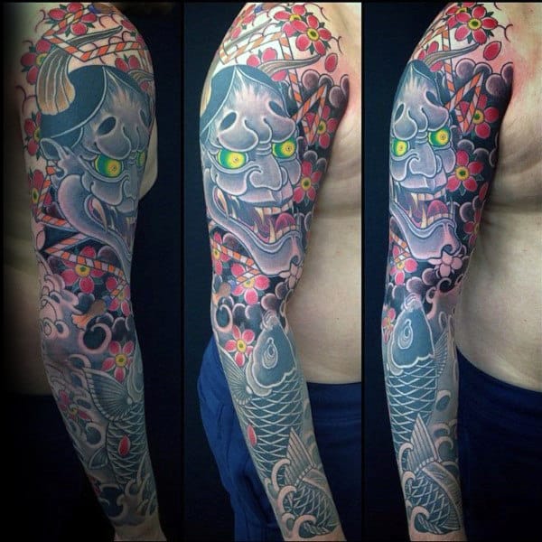 Japanese-style full sleeve tattoo featuring a fierce blue Hannya mask with glowing green eyes, koi fish, swirling waves, and pink cherry blossoms