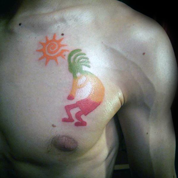 Colorful Kokopelli chest tattoo in red, orange, and green with a matching spiral sun symbol, giving a vibrant and playful energy.