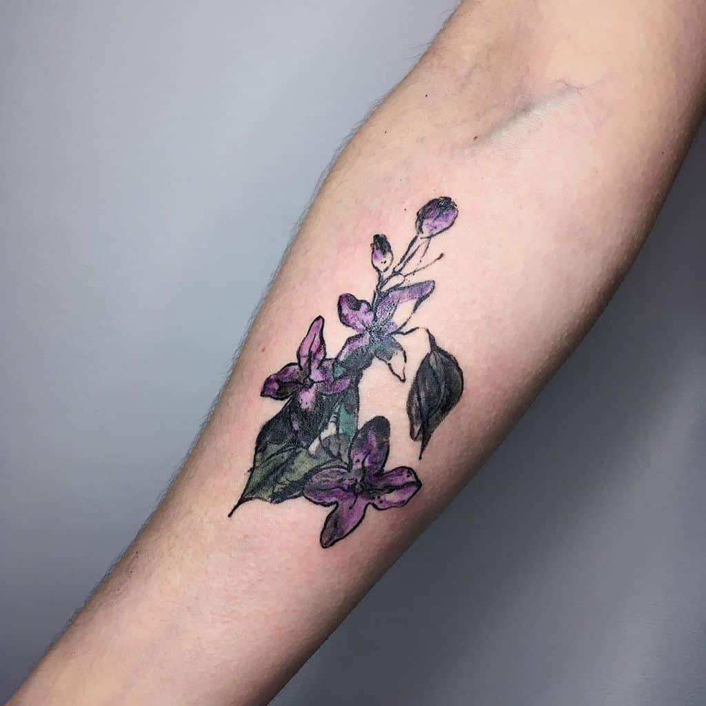 Artistic forearm tattoo of a lilac branch with deep purple flowers and dark leaves, blending watercolor and fine-line techniques.