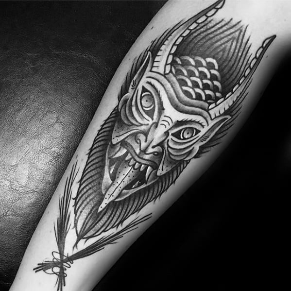 Detailed black and grey Krampus tattoo featuring a fierce horned face with textured scales, sharp teeth, and birch branches below.