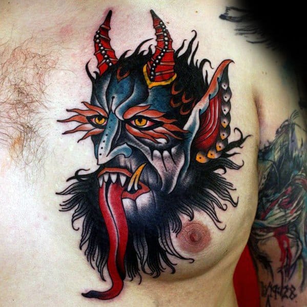Colorful Krampus tattoo on chest with a blue and red horned face, glowing yellow eyes, sharp fangs, and a flowing red tongue.
