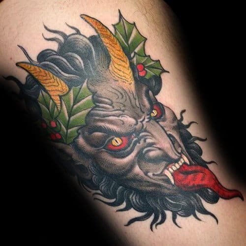 Krampus tattoo with a snarling grey face, fiery eyes, yellow horns, red tongue, and holly leaves for a dark festive look.