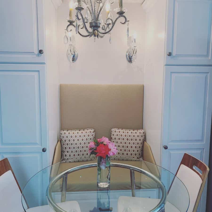 Country-style dining area with a high-backed banquette, glass round table, and elegant chandelier.