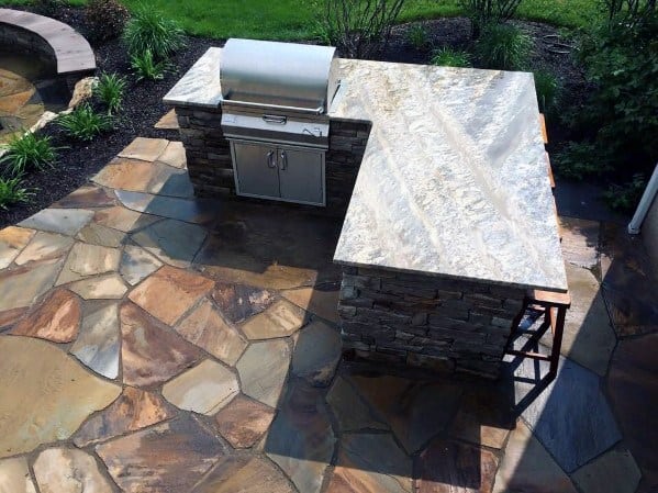 Outdoor stone patio featuring a built-in grill with granite countertop, surrounded by lush greenery