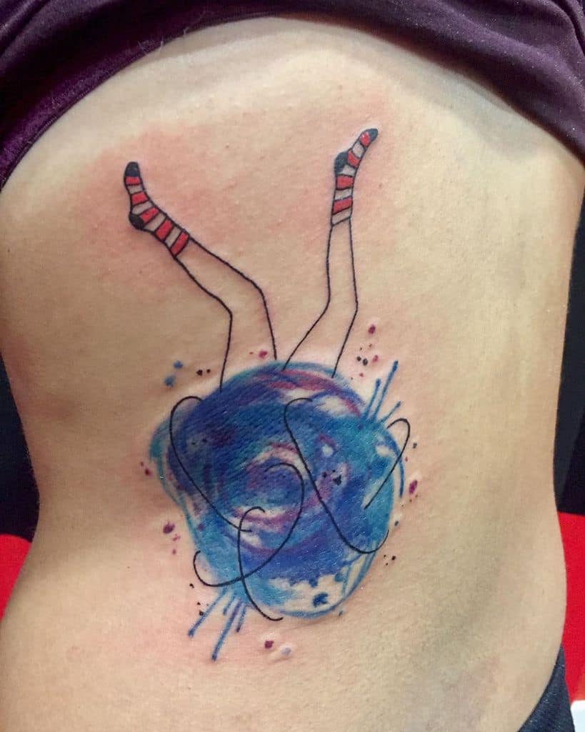 A colorful tattoo of a person falling into a swirling galaxy, with only their legs visible wearing striped socks, blending surreal and cosmic themes.