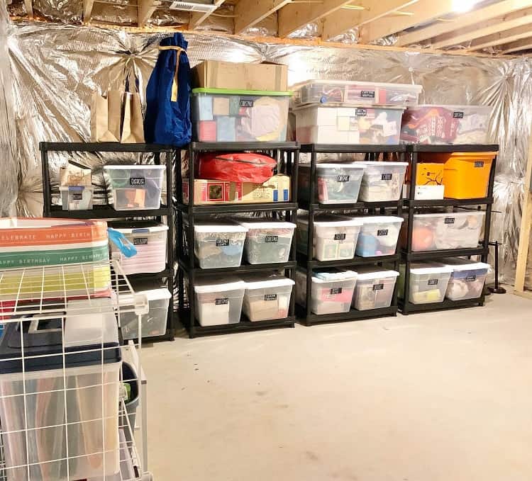 Basement shelves with labeled clear bins storing household items in an unfinished space.