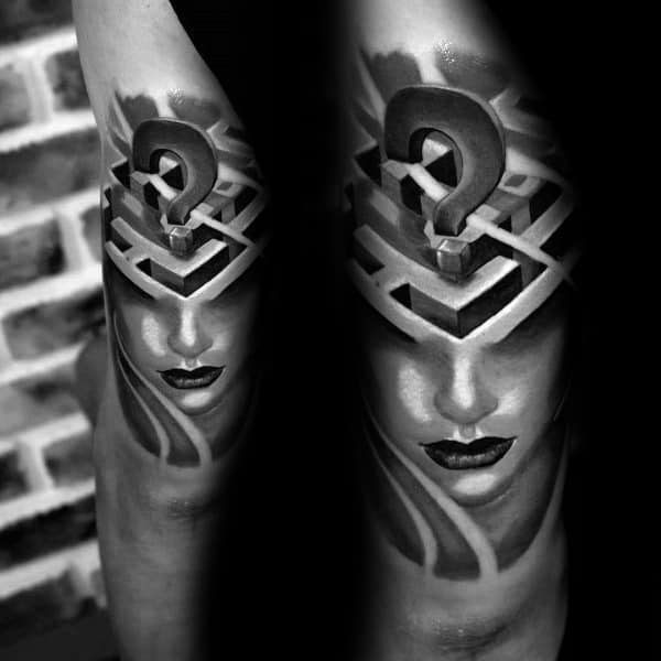 Realistic black and grey tattoo on a man's arm, featuring a woman's face with a 3D labyrinth on her forehead and a question mark above.