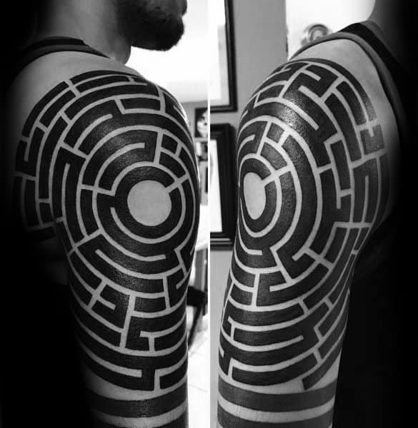 Bold blackwork labyrinth tattoo covering a man's upper arm and shoulder, featuring a circular maze design with thick, geometric lines.