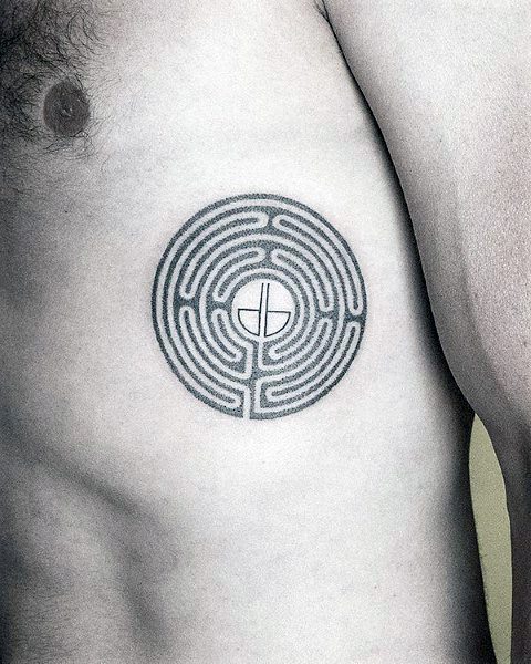 Minimalist circular labyrinth tattoo on a man's ribcage, featuring a clean maze design with a small plant symbol at the center.