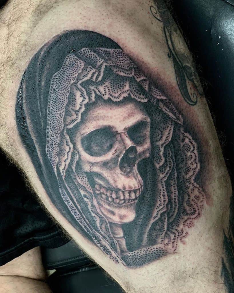 Realistic black and grey tattoo of a skull draped in intricate lace and a hood, creating a haunting yet detailed gothic-inspired design.