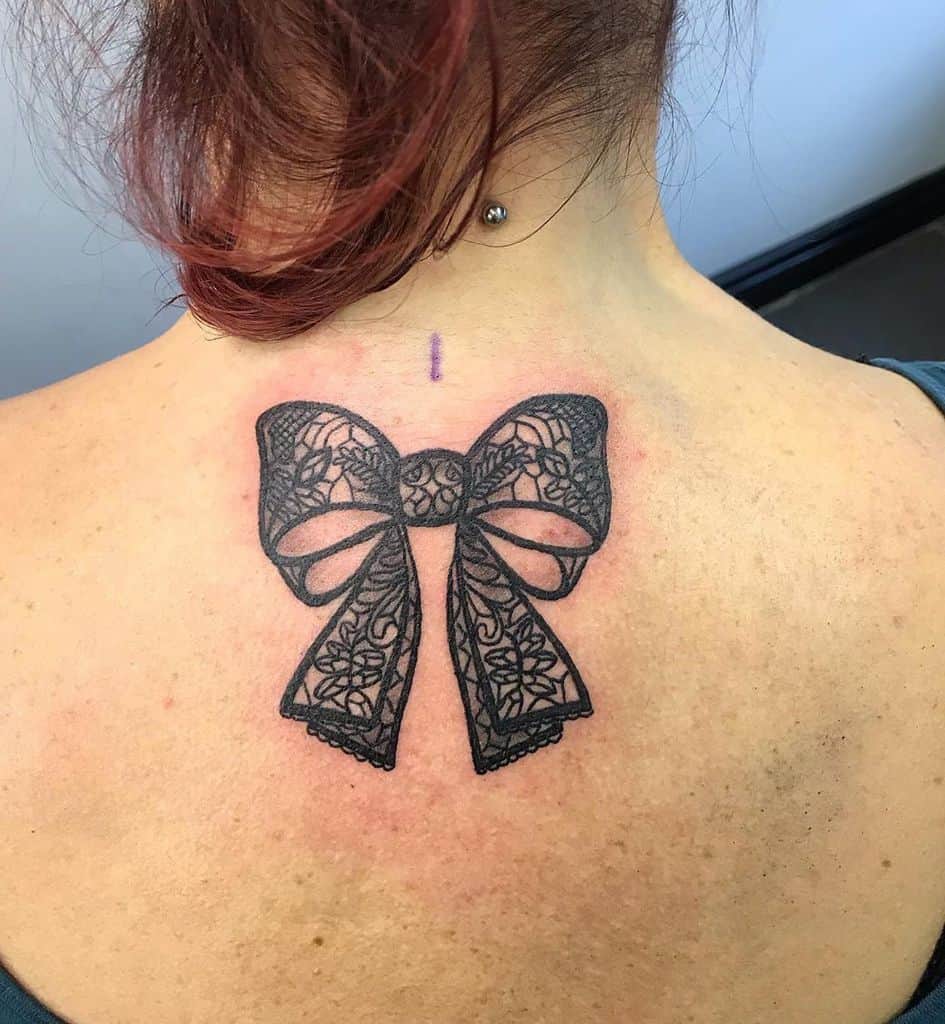 Black lace bow tattoo on the upper back, featuring intricate floral patterns for an elegant and delicate design.