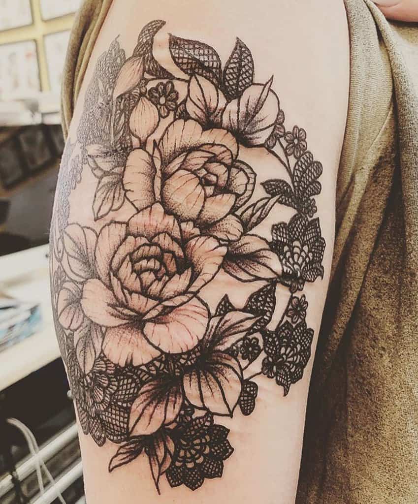 Elegant upper arm tattoo featuring detailed roses surrounded by intricate lace patterns and floral accents for a delicate, feminine look.