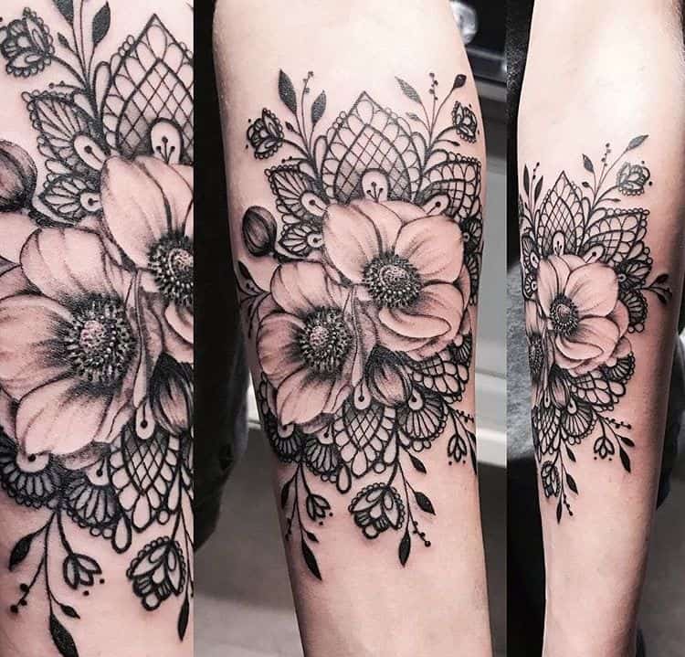 Elegant forearm tattoo featuring realistic shaded flowers with intricate black lace patterns, ornamental swirls, and delicate details.