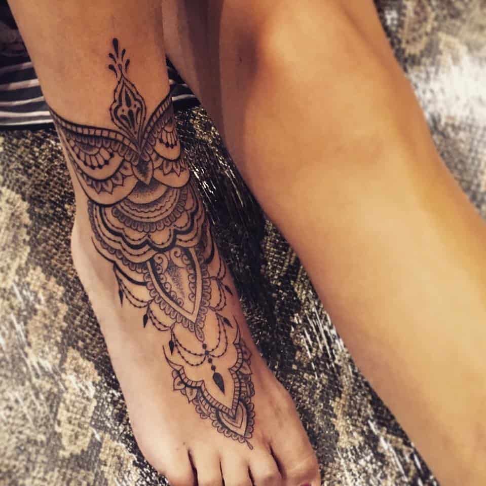 Elegant foot and ankle tattoo featuring intricate lace patterns, ornamental filigree, and delicate mandala-style details.