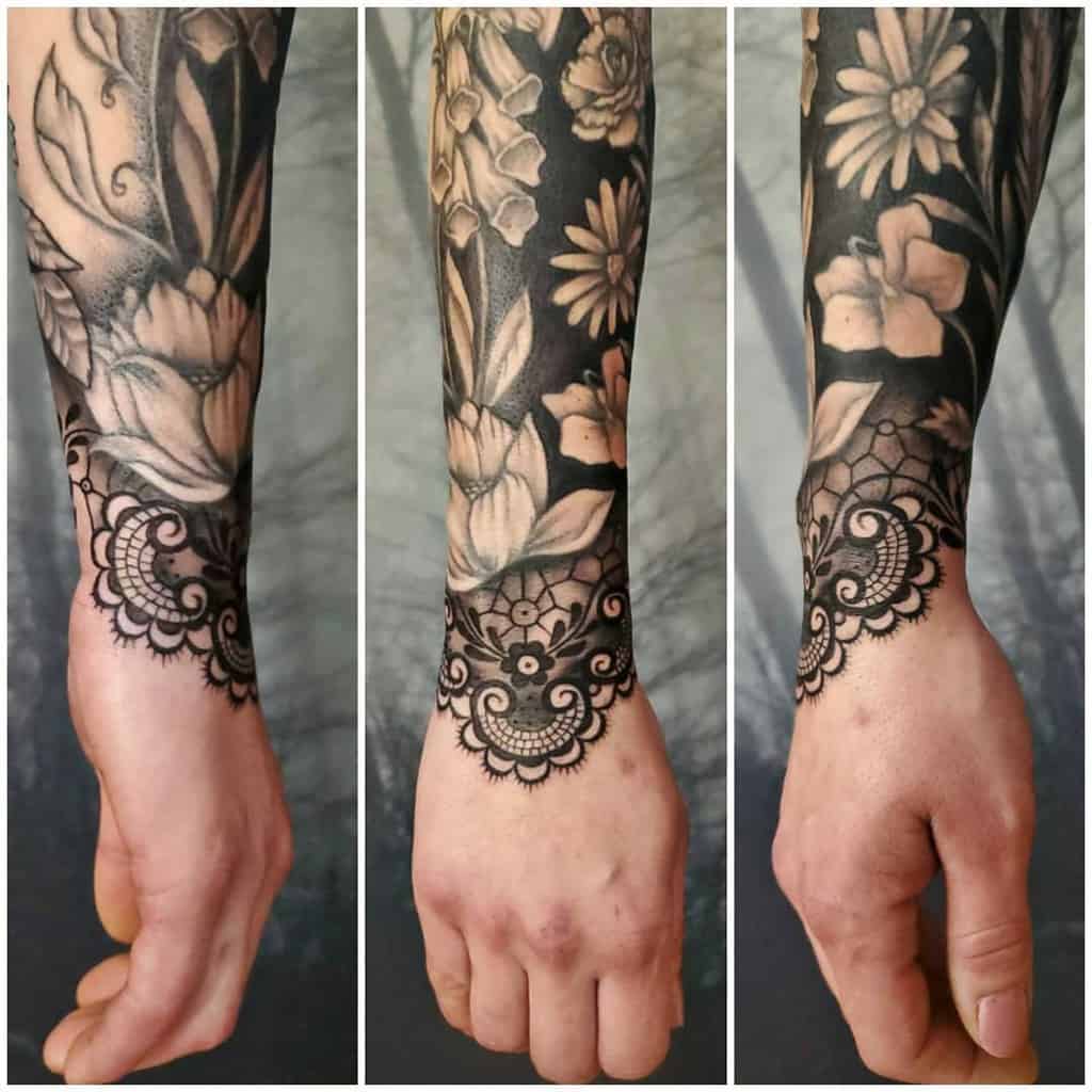 Black and grey floral sleeve tattoo with intricate lace cuff details on the wrist, blending soft shading with bold ornamental patterns.