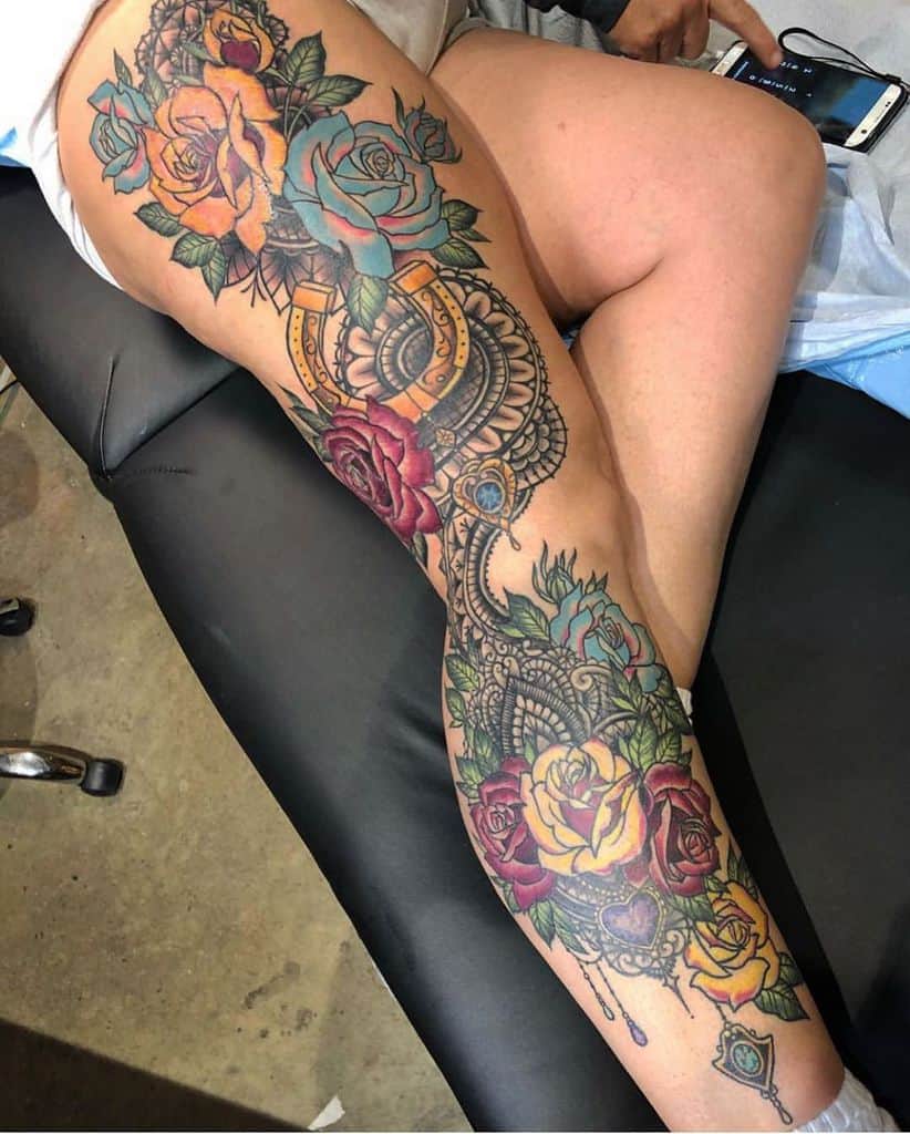 Vibrant full-leg tattoo featuring colorful roses, intricate lace details, a golden horseshoe, and ornamental gemstones for a bold look.