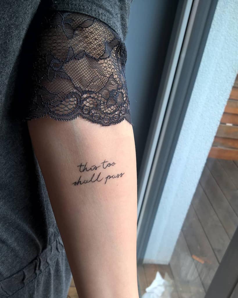 A "This Too Shall Pass" tattoo in cursive on a person's arm.