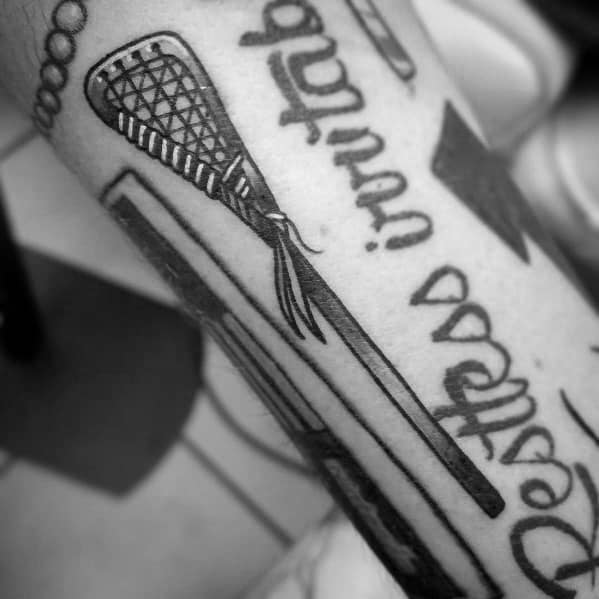 Bold black ink lacrosse stick tattoo with fine netting details, integrated into a larger design on the forearm for a striking athletic look.
