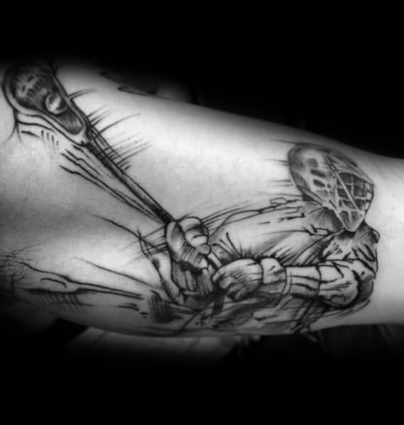 Dynamic black and grey lacrosse tattoo featuring a masked player gripping a lacrosse stick, with bold shading and motion lines for intensity.
