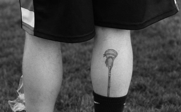 Minimalist lacrosse stick tattoo with fine line details, placed on the calf for a subtle yet meaningful tribute to the sport.
