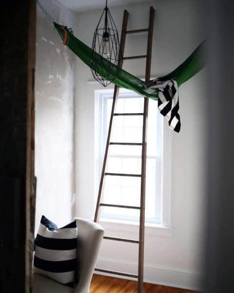 Green hammock in a minimalist room with a wooden ladder and striped decor accents.