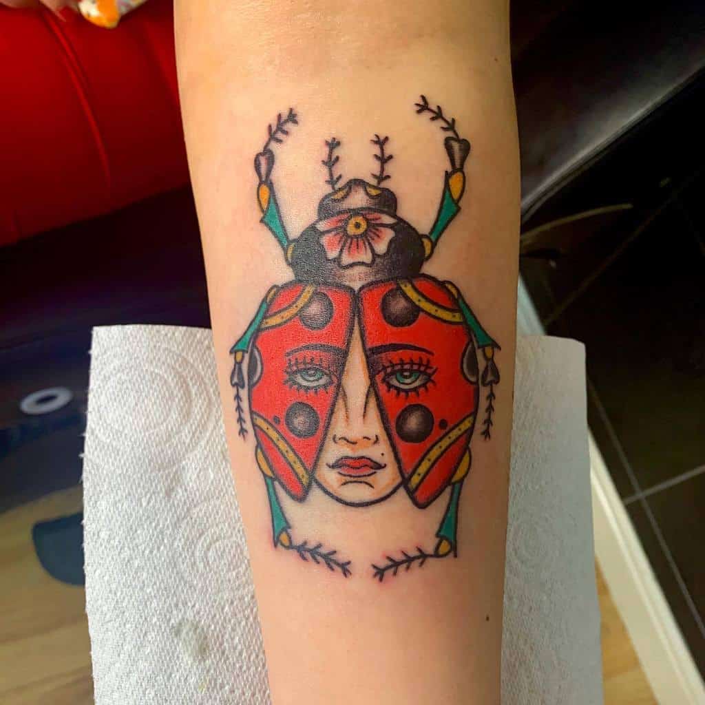 Neo-traditional ladybug tattoo with a surreal twist, featuring a woman's face within its wings, bold colors, and intricate detailing for a unique design.