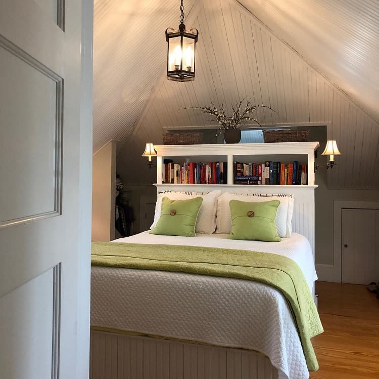 Cozy attic bedroom with a white bed, green accents, bookshelves, and warm lighting under a charming ceiling