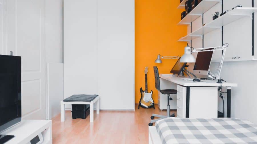 Small bedroom with an orange feature wall, computer desk, and guitar setup.