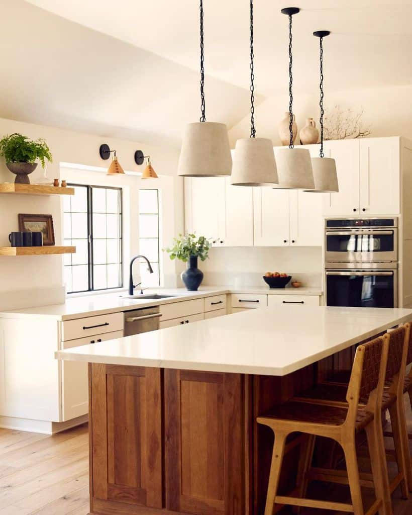 Bright kitchen with wooden island woven barstools white cabinets and large pendant lights.