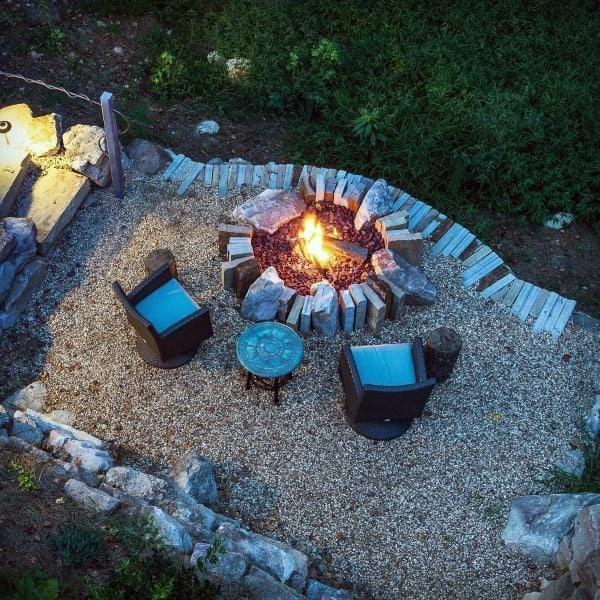 Aerial view of a fire pit with three chairs and a table on gravel, surrounded by lush greenery