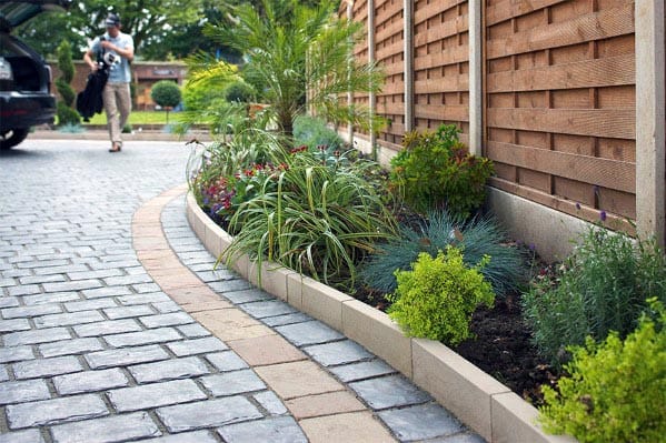 Cobblestone driveway with curved concrete edging and a vibrant landscaped border.