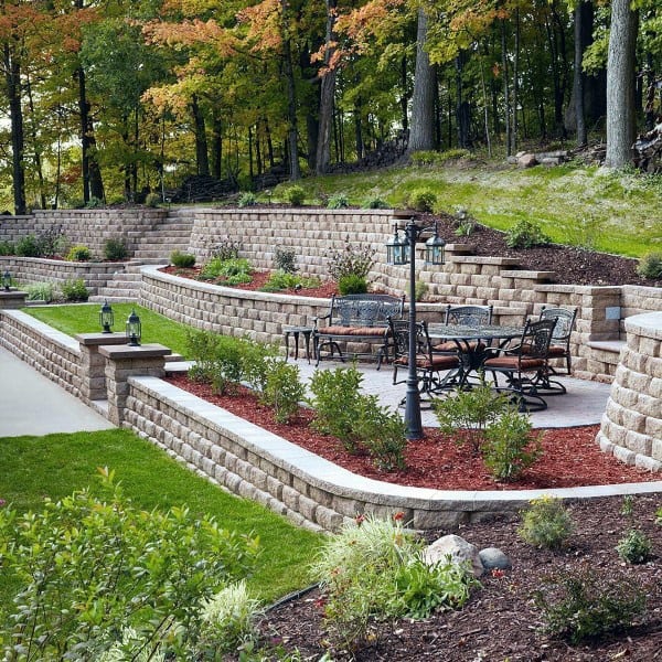 Tiered brick retaining walls with landscaped beds, patio furniture, and a lamp post.