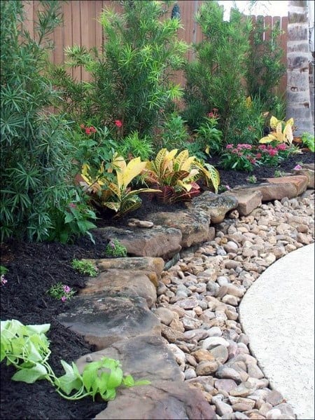 A garden bed bordered with stone edging, featuring lush plants and vibrant flowers, creating a neat and inviting landscape
