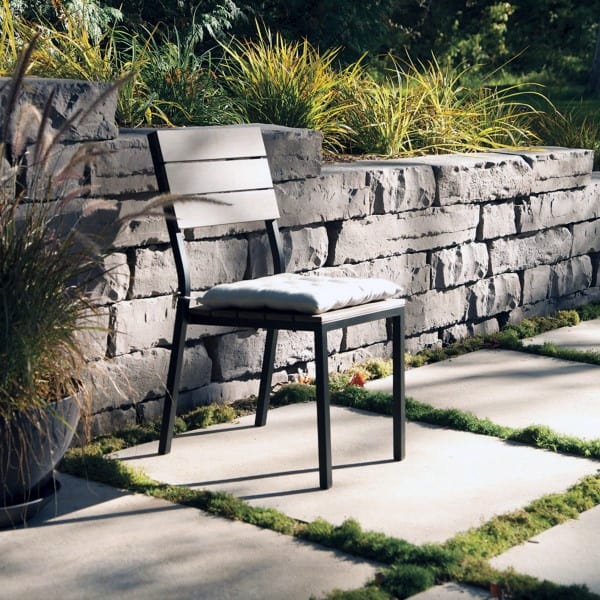 Modern patio chair with cushion beside a stone retaining wall and lush greenery.