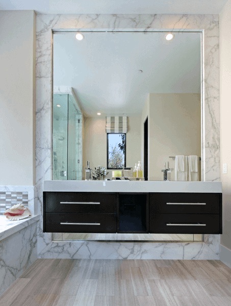 Modern bathroom with large recessed mirror, marble walls, and floating vanity.