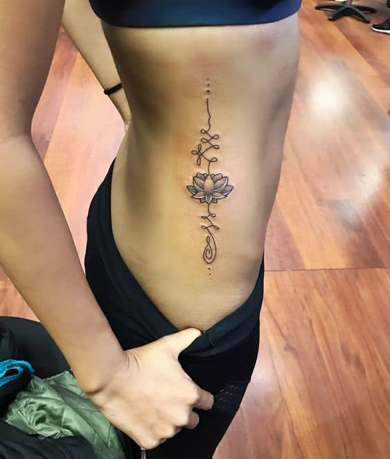 Unalome tattoo with a lotus on the side torso, symbolizing spiritual growth, resilience, and the journey toward enlightenment and inner peace.