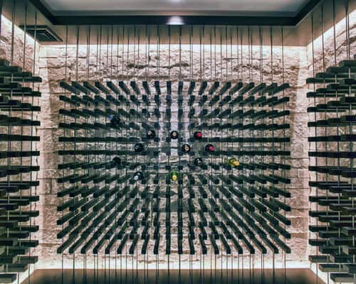 Wine bottles rest horizontally on a wall-mounted rack against a backlit stone backdrop, creating a wine lover's dream