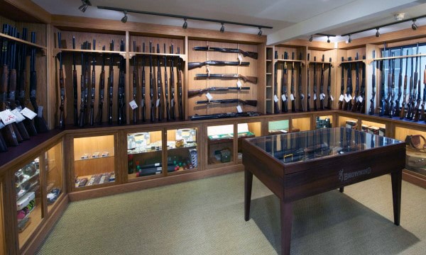 Elegant gun room with wooden display racks, glass cases, and a central showcase table.