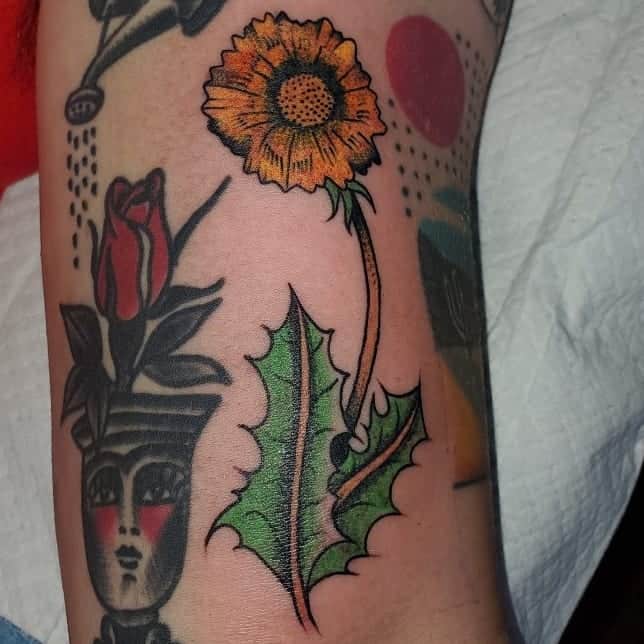 This tattoo showcases a bright sunflower paired with bold, colorful leaves, creating a striking, dynamic design.