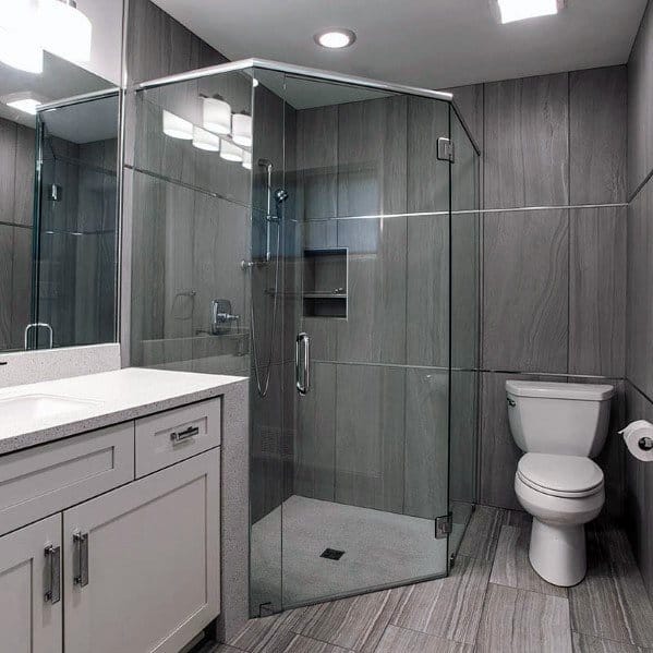 Modern bathroom with a corner glass shower, gray tile walls, white cabinets, and a toilet