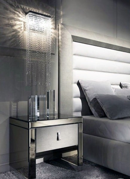 Luxury gray bedroom with mirrored nightstand and crystal chandelier wall sconce.