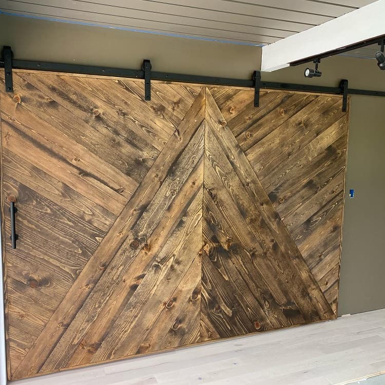 Large rustic sliding barn door with chevron wood pattern and matte metal hardware.