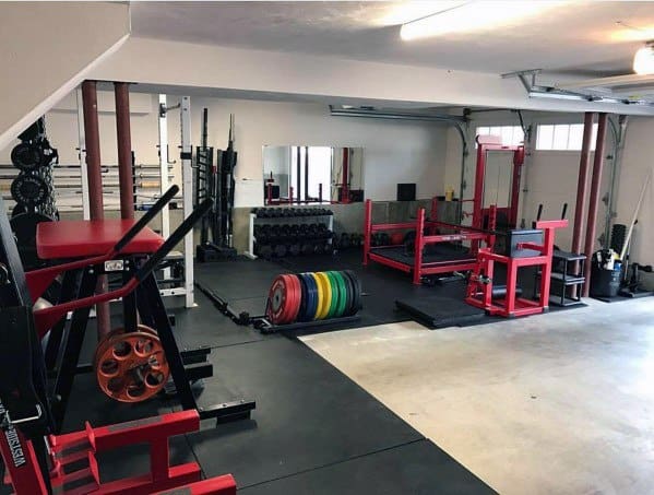 Spacious garage gym with red equipment, weightlifting platforms, dumbbells, and barbell storage.