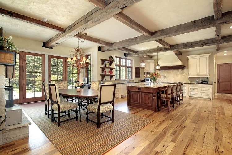 Spacious kitchen with wooden beams, large windows, hardwood floors, patterned chairs, and a high ceiling