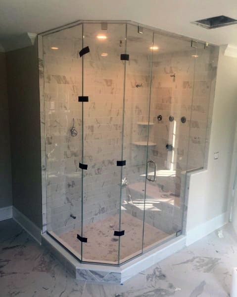 Corner glass-enclosed shower with marble tile walls and floor, featuring a rainfall showerhead