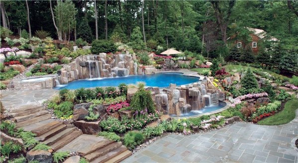 Luxury backyard pool with cascading waterfall, surrounded by lush greenery, flowers, and a stone patio