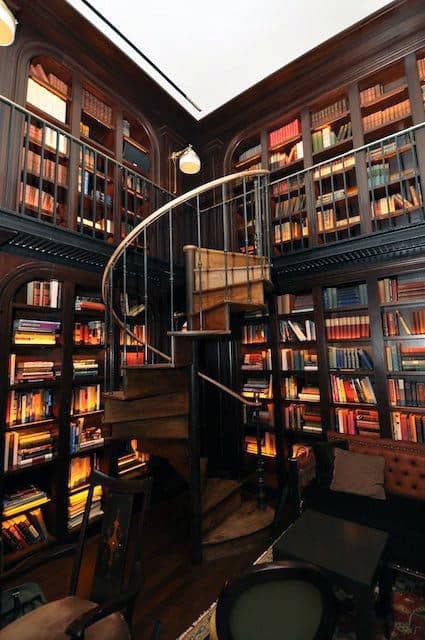 A cozy, dark wood library with a spiral staircase, bookshelves bursting with reads, and warm lighting