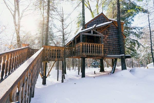 Treehouse cabin surrounded by snowy woods, with sunlight filtering through the trees